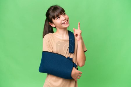 Photo for Little caucasian girl with broken arm and wearing a sling over isolated background pointing up a great idea - Royalty Free Image