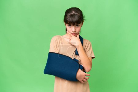 Photo for Little caucasian girl with broken arm and wearing a sling over isolated background thinking - Royalty Free Image