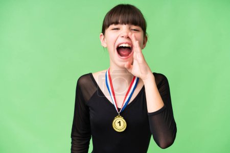 Foto de Pequeña chica caucásica con medallas sobre fondo aislado gritando con la boca abierta - Imagen libre de derechos