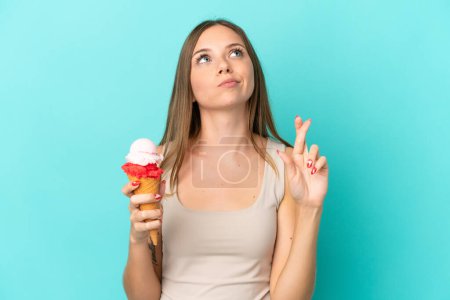 Photo for Young Lithuanian woman with cornet ice cream isolated on blue background with fingers crossing and wishing the best - Royalty Free Image