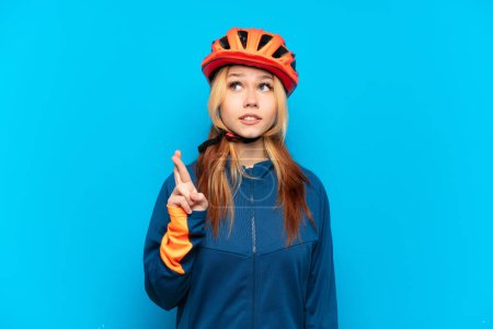 Téléchargez les photos : Jeune cycliste fille isolée sur fond bleu avec les doigts croisés et souhaitant le meilleur - en image libre de droit