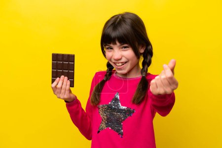 Téléchargez les photos : Petite fille caucasienne au chocolat isolé sur fond jaune faisant geste d'argent - en image libre de droit