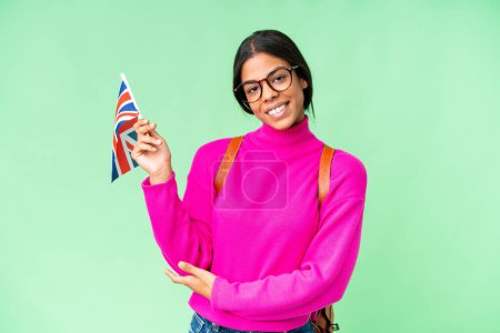 Téléchargez les photos : Jeune femme afro-américaine tenant un drapeau du Royaume-Uni sur fond isolé chroma clé étendant les mains sur le côté pour inviter à venir - en image libre de droit