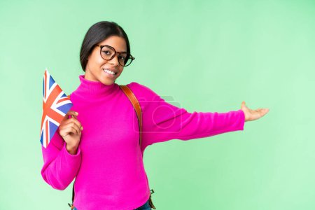 Téléchargez les photos : Jeune femme afro-américaine tenant un drapeau du Royaume-Uni sur fond isolé chroma clé étendant les mains sur le côté pour inviter à venir - en image libre de droit