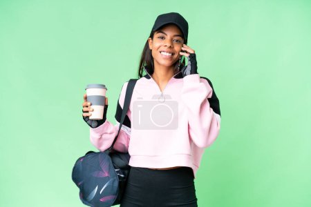 Photo pour Jeune femme afro-américaine sportive avec sac de sport sur fond isolé chroma clé tenant café à emporter et un mobile - image libre de droit