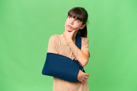 Photo for Little caucasian girl with broken arm and wearing a sling over isolated background having doubts - Royalty Free Image