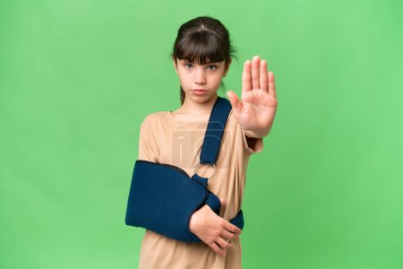 Photo for Little caucasian girl with broken arm and wearing a sling over isolated background making stop gesture - Royalty Free Image