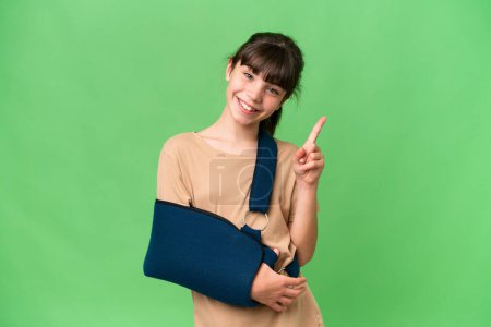 Little caucasian girl with broken arm and wearing a sling over isolated background showing and lifting a finger in sign of the best
