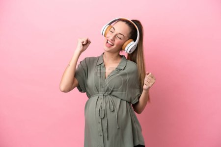 Foto de Mujer joven aislada sobre fondo rosa embarazada y escuchando música - Imagen libre de derechos
