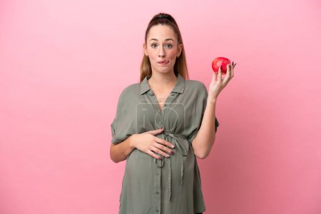 Photo for Young woman isolated on pink background pregnant and holding an apple - Royalty Free Image