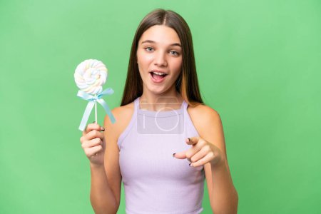 Foto de Adolescente caucásico chica sosteniendo una piruleta sobre aislado fondo sorprendido y apuntando frente - Imagen libre de derechos