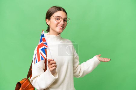 Téléchargez les photos : Adolescente étudiante caucasienne tenant un drapeau du Royaume-Uni sur fond isolé étendant les mains sur le côté pour inviter à venir - en image libre de droit