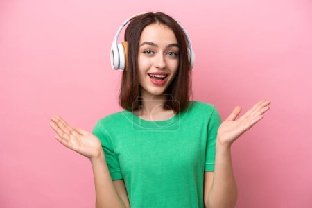 Young Ukrainian woman isolated on pink background surprised and listening music
