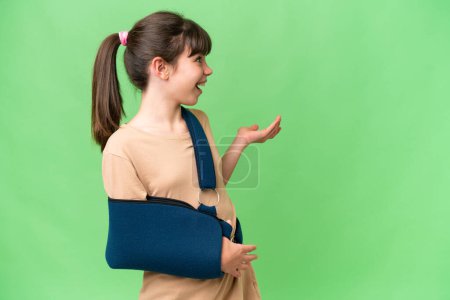 Photo for Little caucasian girl with broken arm and wearing a sling over isolated background with surprise expression while looking side - Royalty Free Image