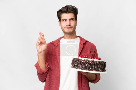 Photo for Young caucasian man holding birthday cake over isolated background with fingers crossing and wishing the best - Royalty Free Image