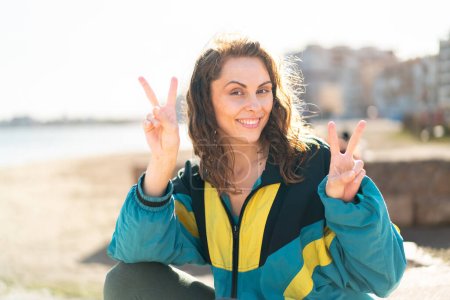 Photo for Young sport woman at outdoors showing victory sign with both hands - Royalty Free Image