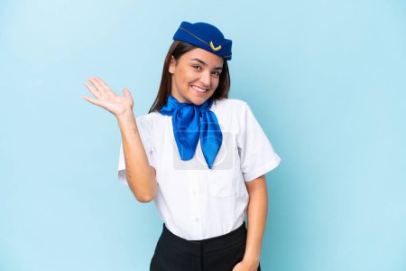 Azafata de avión mujer caucásica aislada sobre fondo azul saludando con la mano con expresión feliz