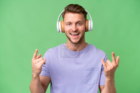 Young blonde caucasian man over isolated background listening music making rock gesture
