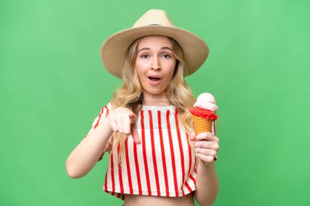 Foto de Joven mujer inglesa con un helado de corneta sobre fondo aislado sorprendido y apuntando hacia delante - Imagen libre de derechos