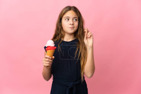 Photo for Child with a cornet ice cream over isolated pink background with fingers crossing and wishing the best - Royalty Free Image