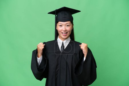 Téléchargez les photos : Jeune diplômée universitaire asiatique sur fond isolé célébrant une victoire en position gagnante - en image libre de droit