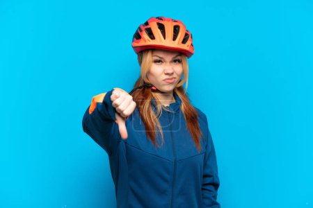 Photo for Young cyclist girl isolated on blue background showing thumb down with negative expression - Royalty Free Image