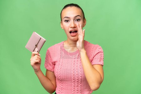 Photo for Young Arab woman holding a wallet over isolated background shouting with mouth wide open - Royalty Free Image