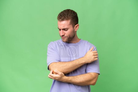 Young handsome caucasian man isolated on green chroma background with pain in elbow