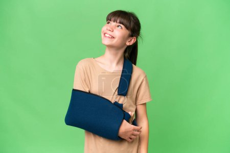 Photo for Little caucasian girl with broken arm and wearing a sling over isolated background thinking an idea while looking up - Royalty Free Image