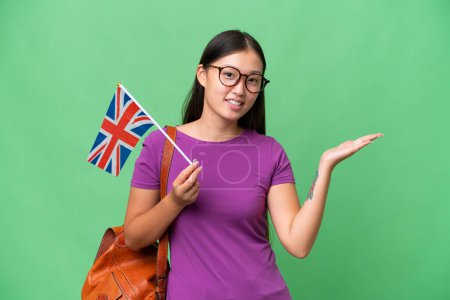 Téléchargez les photos : Young Asian woman holding an United Kingdom flag over isolated background extending hands to the side for inviting to come - en image libre de droit