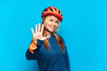 Téléchargez les photos : Jeune cycliste fille isolée sur fond bleu comptant cinq avec les doigts - en image libre de droit