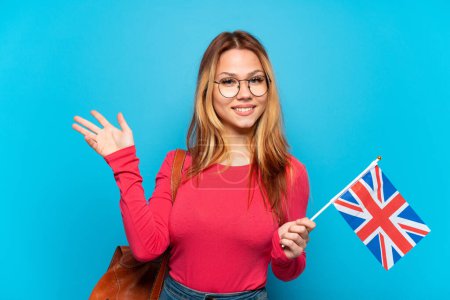 Téléchargez les photos : Jeune fille tenant un drapeau du Royaume-Uni sur fond bleu isolé étendant les mains sur le côté pour inviter à venir - en image libre de droit