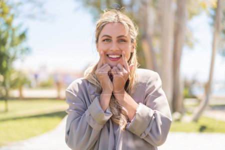 Téléchargez les photos : Jeune jolie femme uruguayenne blonde en plein air souriant avec une expression heureuse et agréable - en image libre de droit