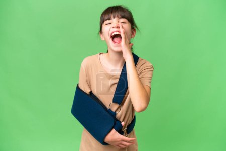 Photo for Little caucasian girl with broken arm and wearing a sling over isolated background shouting with mouth wide open - Royalty Free Image