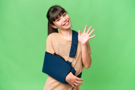 Little caucasian girl with broken arm and wearing a sling over isolated background counting five with fingers
