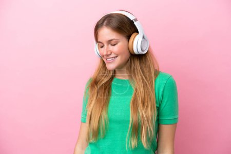 Young blonde woman isolated on pink background listening music