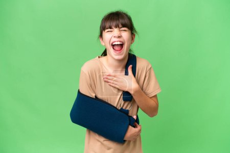 Photo for Little caucasian girl with broken arm and wearing a sling over isolated background smiling a lot - Royalty Free Image