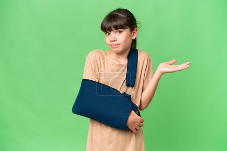 Photo for Little caucasian girl with broken arm and wearing a sling over isolated background having doubts while raising hands - Royalty Free Image