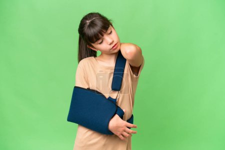 Téléchargez les photos : Petite fille caucasienne avec le bras cassé et portant une fronde sur fond isolé souffrant de douleur à l'épaule pour avoir fait un effort - en image libre de droit