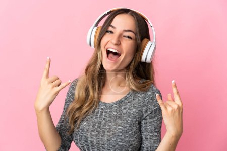 Young Romanian woman isolated on pink background listening music making rock gesture