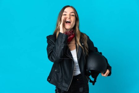 Romanian woman holding a motorcycle helmet isolated on blue background shouting with mouth wide open