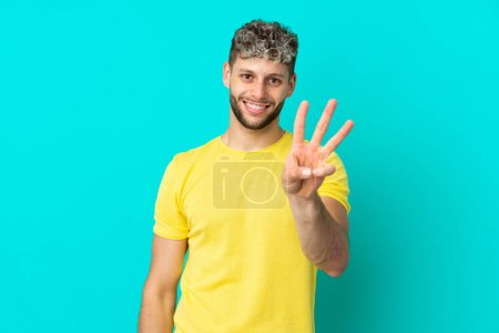 Foto de Joven guapo hombre caucásico aislado sobre fondo azul feliz y contando tres con los dedos - Imagen libre de derechos