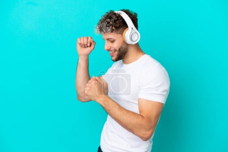 Young handsome caucasian man isolated on blue background listening music and dancing