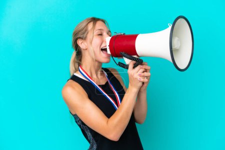 Photo for Young caucasian woman with medals isolated on blue background shouting through a megaphone - Royalty Free Image