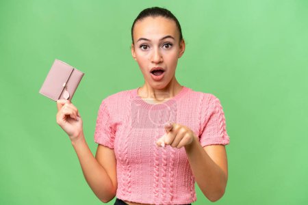 Photo for Young Arab woman holding a wallet over isolated background surprised and pointing front - Royalty Free Image