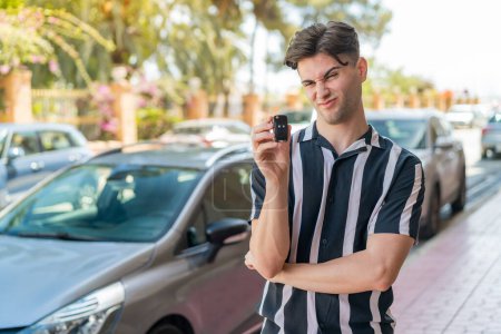 Téléchargez les photos : Jeune homme beau tenant des clés de voiture à l'extérieur avec une expression triste - en image libre de droit