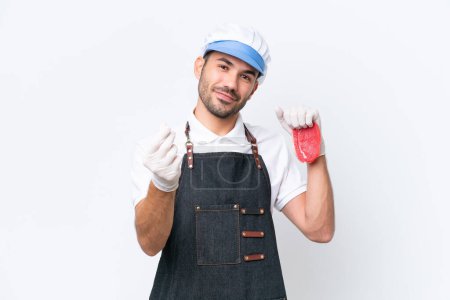 Téléchargez les photos : Boucher homme caucasien portant un tablier et servir de la viande fraîche coupée sur fond blanc isolé faisant geste d'argent - en image libre de droit