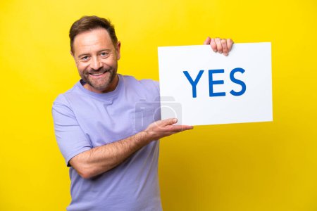 Téléchargez les photos : Middle age caucasian man isolated on yellow background holding a placard with text YES with happy expression - en image libre de droit