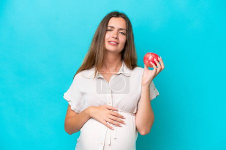 Photo for Young caucasian woman isolated on blue background pregnant and frustrated while holding an apple - Royalty Free Image