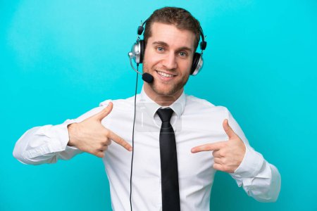 Telemarketer caucasian man working with a headset isolated on blue background proud and self-satisfied
